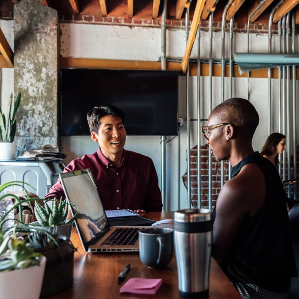 Man and woman having a conversation over their computers in a trendy, industrial coffee shop.